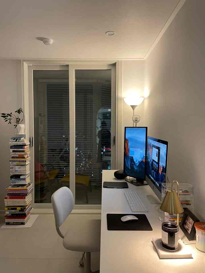 白を基調とした書斎兼ホームオフィス、デュアルモニターと多くの本がある作業空間