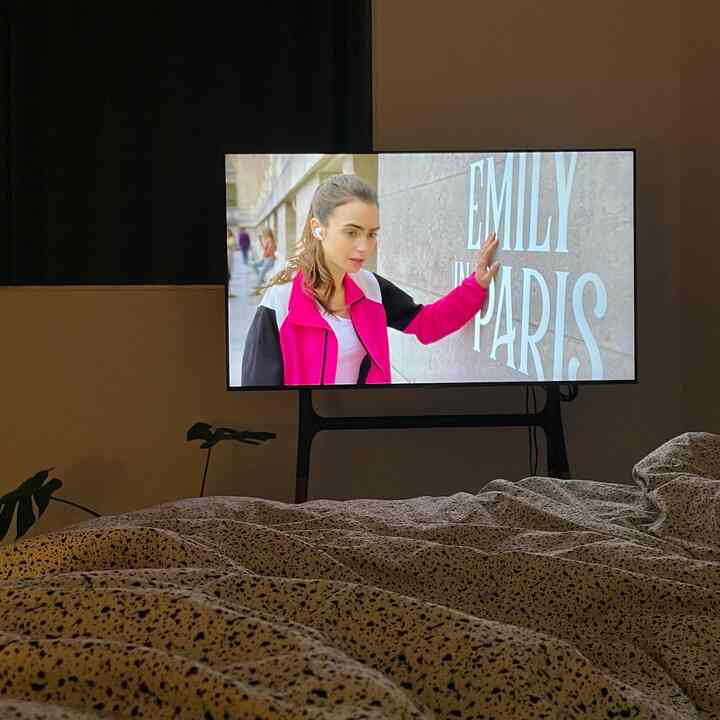 ダークなブラックカーテンとベージュの寝具が配置された寝室、中央のテレビ台にテレビが置かれた雰囲気のあるインテリア