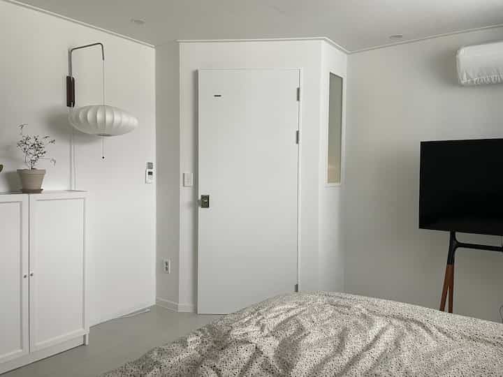 白を基調とした寝室、独特な間取りとモダンな雰囲気のテレビ台とイケア収納が配置された空間