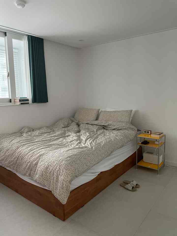 白と茶色のトーンの寝室、木製ベッドフレームと柄付き寝具、黄色のナイトテーブルが配置されたシンプルな空間