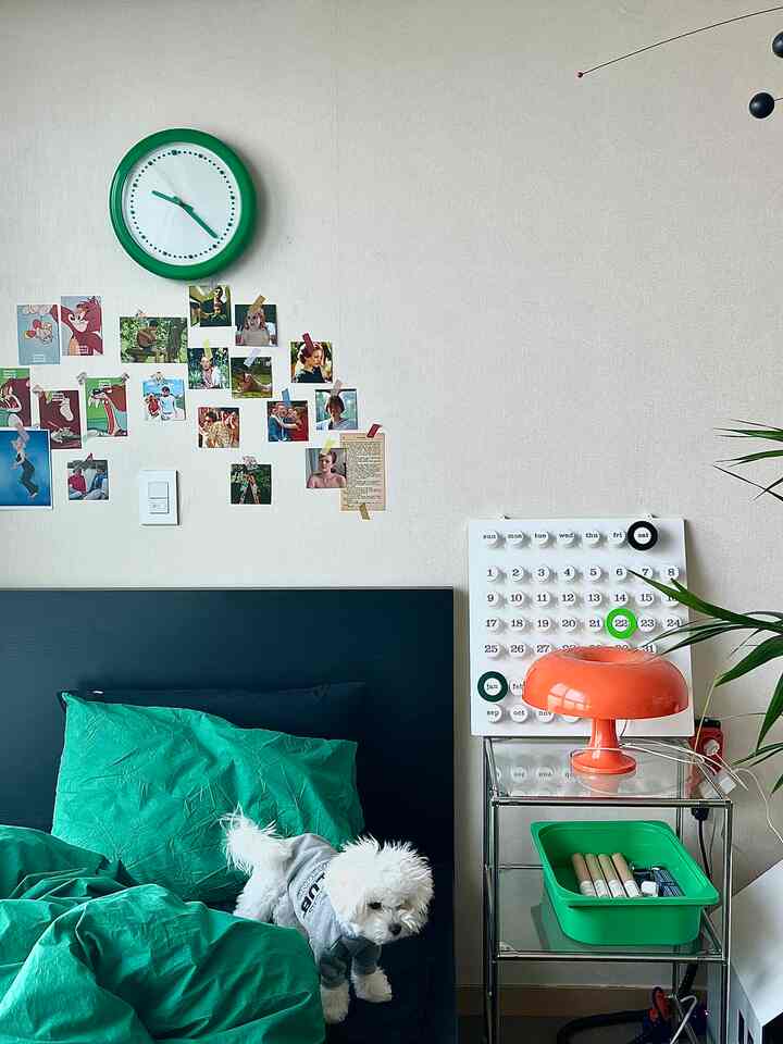 グリーントーンの寝室、黒いベッドとヴィンテージポスターの壁装飾、オレンジ色のテーブルランプが配置された温かみのある空間