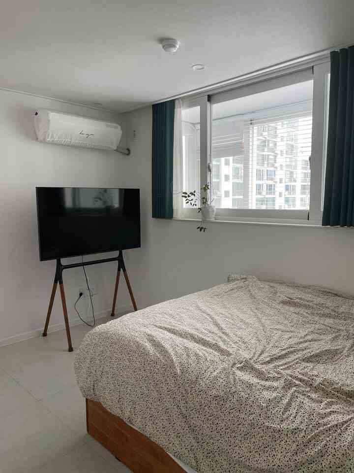 白を基調とした寝室、木製ベッドフレームとテレビ台が配置されたモダンなインテリア