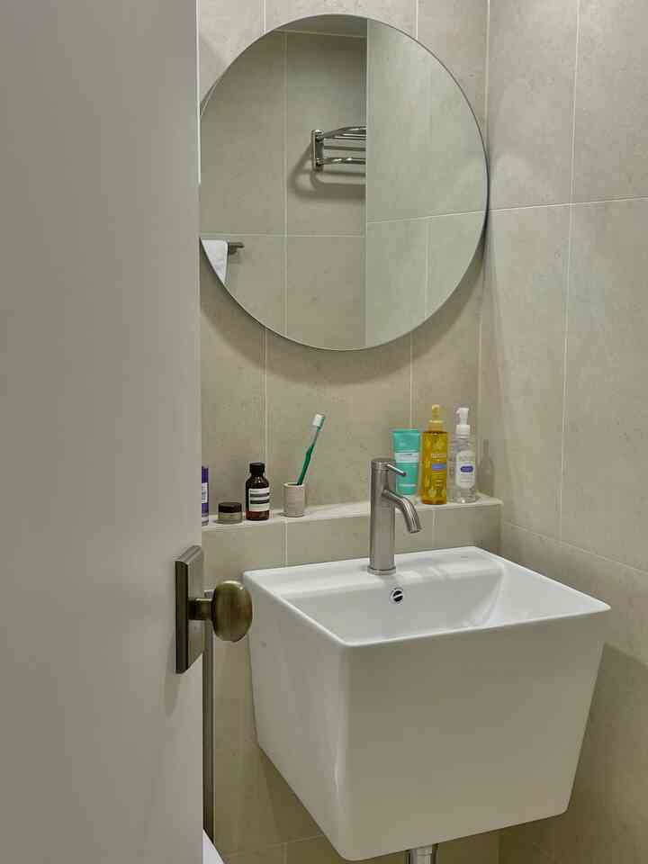 ベージュのタイル壁と白い洗面台、丸い鏡が配置されたシンプルなバスルーム