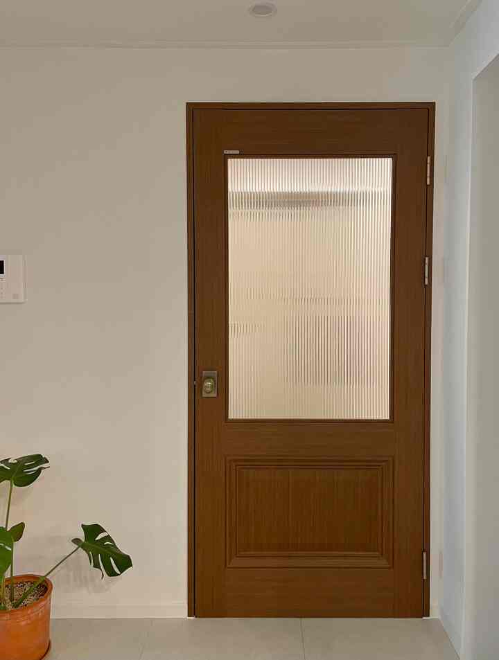 白い壁と明るい床が調和する玄関、木目調の中ドアと縞模様ガラスが配置された自然な雰囲気のインテリア