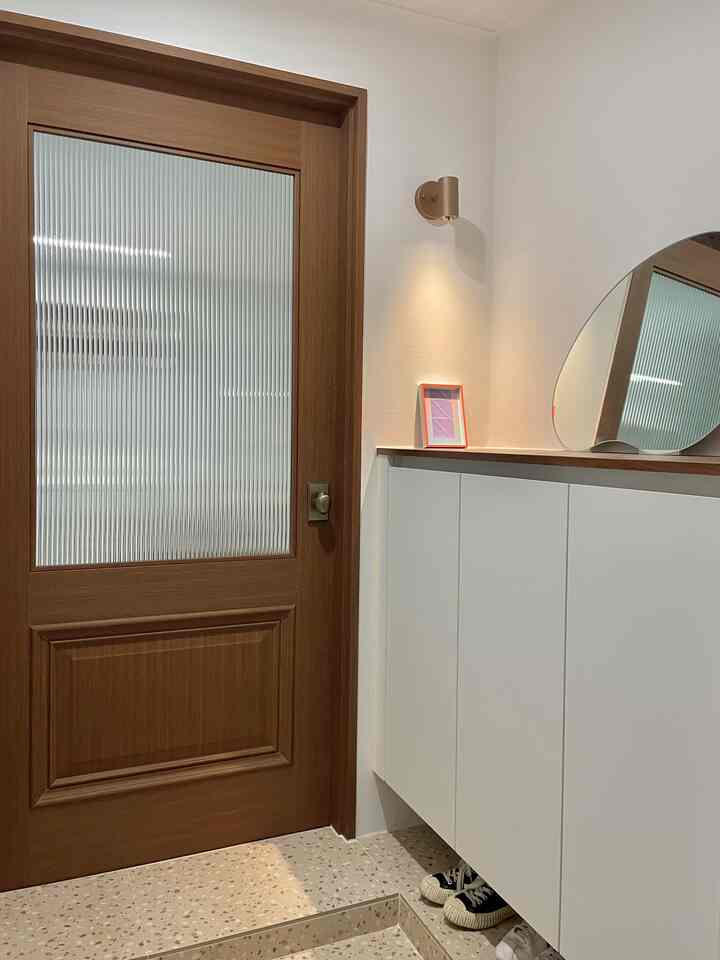 木目調の玄関、白いシューズラックとモルガラスのドアが配置されたシンプルで清潔感のあるインテリア