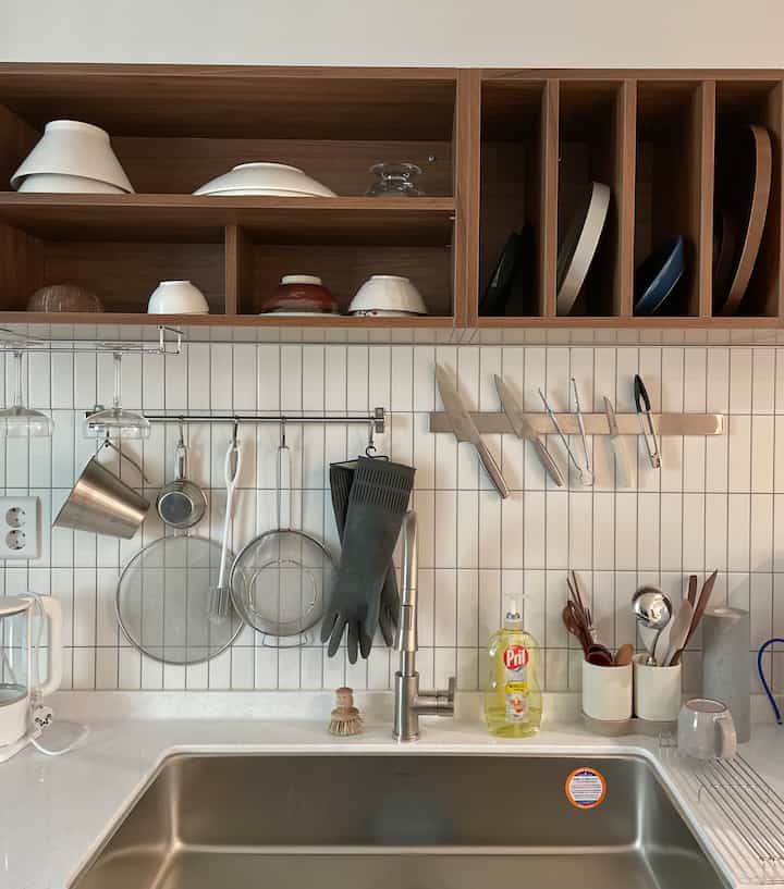 白いタイルの壁と木製棚、ステンレスシンクが配置されたシンプルでナチュラルなキッチン