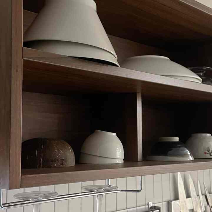 ナチュラルな木目調の上部収納棚に様々なサイズのボウルが整然と並ぶキッチンの収納空間