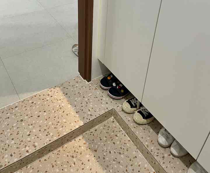 ベージュとブラウンの色調の玄関、テラゾータイルの床と白いシューズラックが配置された清潔感のある空間