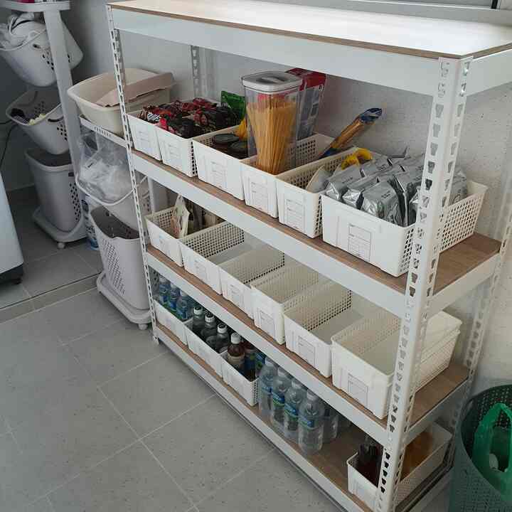 白と木目調のベランダパントリー、整理された収納ボックスと多様な食料品が整然と並ぶ雰囲気のあるインテリア