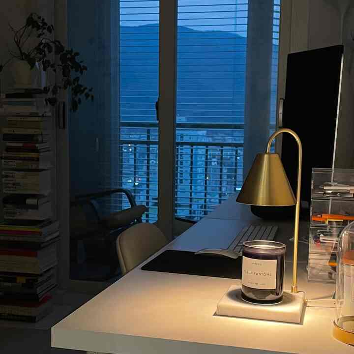 青みがかった夕暮れの書斎、白いデスクにゴールドのテーブルランプとキャンドルが置かれた雰囲気のあるインテリア