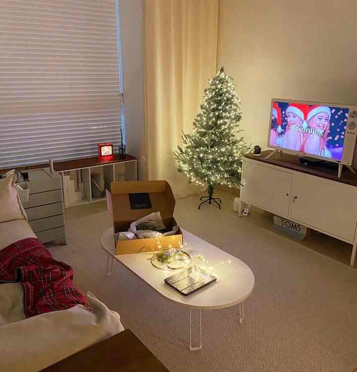 ベージュとホワイトのトーンのリビング、柔らかく灯るクリスマスツリーと居心地の良いソファ、コーヒーテーブルが配置された自然なモダンなインテリアの空間