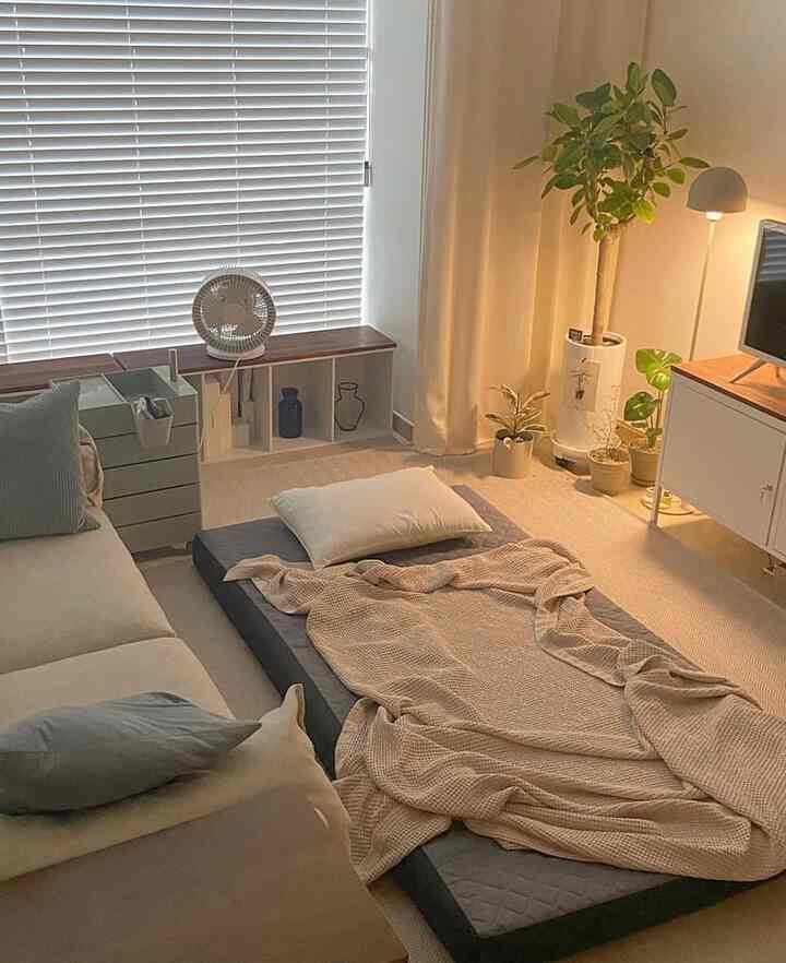 ベージュとナチュラルな色調のリビング兼寝室、ソファと床のマットレスにブランケットとクッションが配置された居心地の良いインテリア