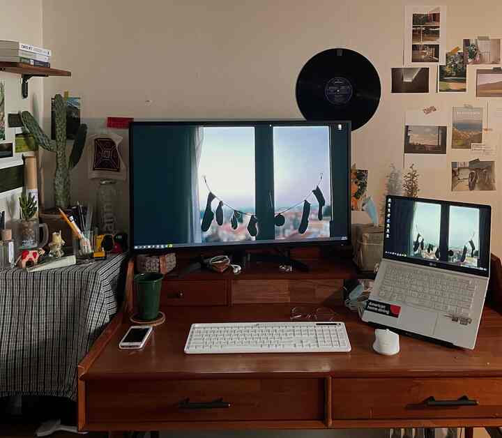 ブラウンの木製デスクを中心に据えた一人暮らしのホームオフィス、白いキーボードとモニターが整った作業環境を演出