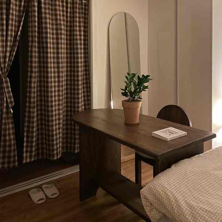 ダークウッドのテーブルとベージュのチェックカーテンが配置されたナチュラル感のある寝室