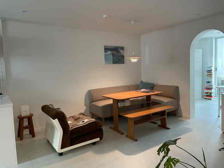 ホワイトとベージュのトーンのリビング、ナチュラルウッドのダイニングテーブルとアームチェアが配置された落ち着いた空間