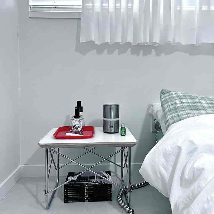 明るいホワイトトーンの寝室、金属フレームのナイトテーブルとチェック柄の枕が調和したモダンでシンプルな空間