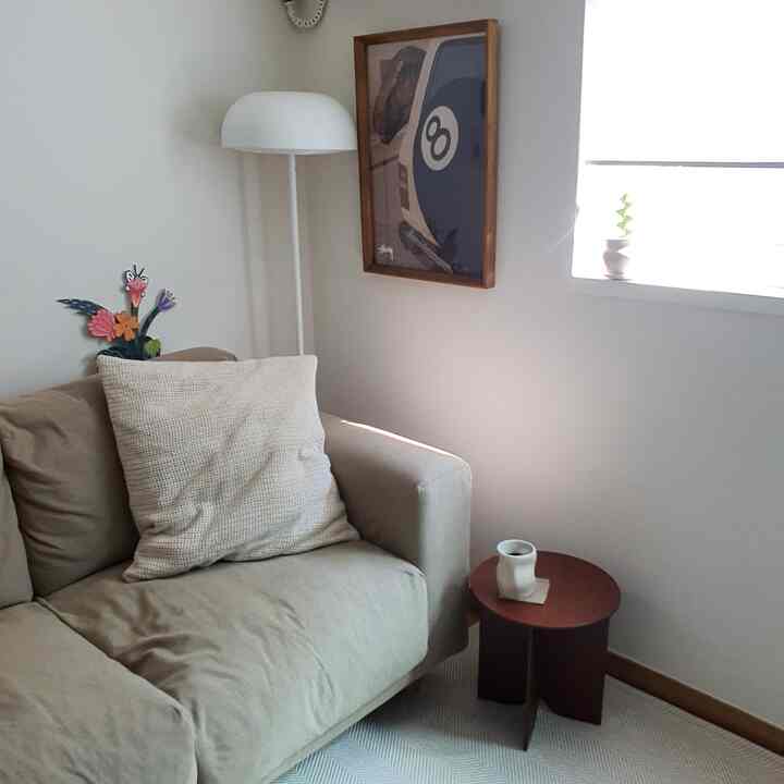 白とベージュのトーンのリビング、ベージュのソファと木製の額縁アート、フロアランプが配置されたシンプルでナチュラルなインテリア