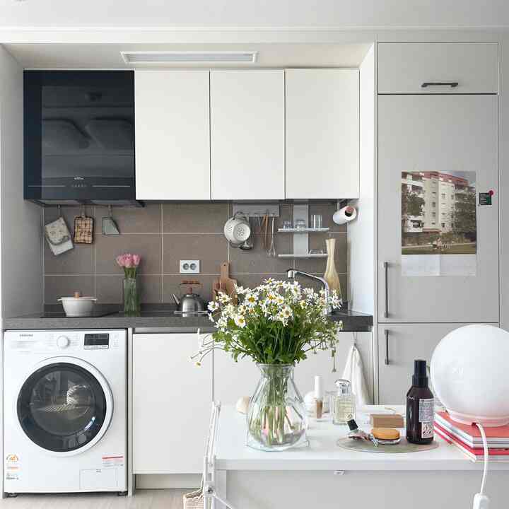 白とベージュのトーンのワンルームキッチン、ガラスの花瓶と花が配置され、整頓されたキッチン用品がある雰囲気のあるインテリア