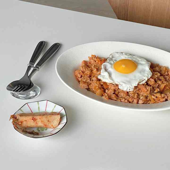 明るい白いダイニングテーブルに目玉焼きが乗ったチャーハンとキムチの小皿が置かれたシンプルな食事風景