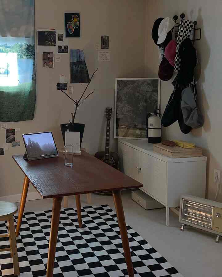 ブラウンのテーブルと白いキャビネットがあるモダンなホームオフィス空間、チェッカーフラッグのラグと多彩な壁の飾りが印象的な部屋