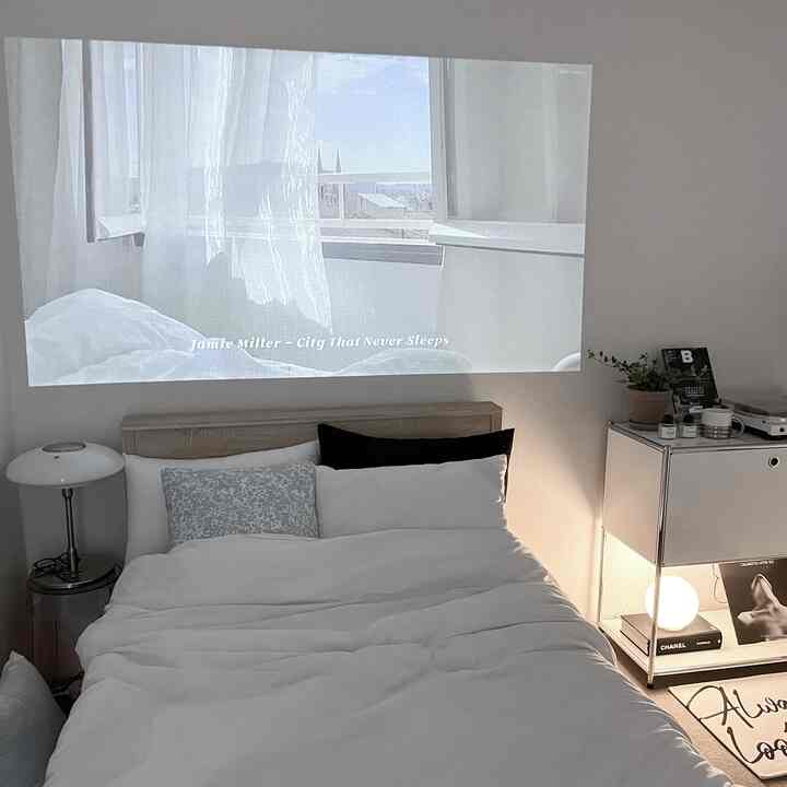明るいホワイトとグレーのトーンの寝室、ミニマルなベッドと壁に投影されたプロジェクター映像のある雰囲気の良いインテリア