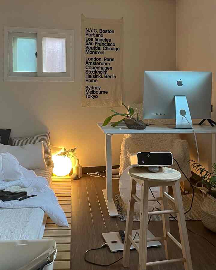 ダークブラウンの床と白い壁、コンピューターデスクと木製のスツールがあるミニマルでナチュラルなワンルームのホームオフィス兼寝室のインテリア