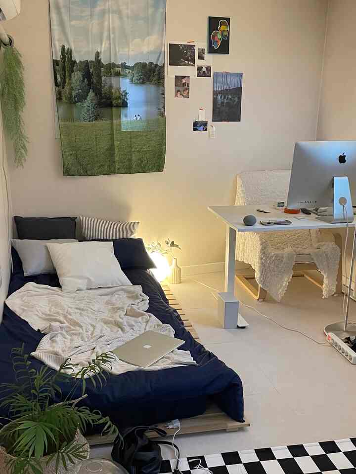 白とネイビーの色調の寝室と在宅勤務用ホームオフィス、木製ベッドベースとチェッカーボード柄のラグが配置された落ち着いた空間