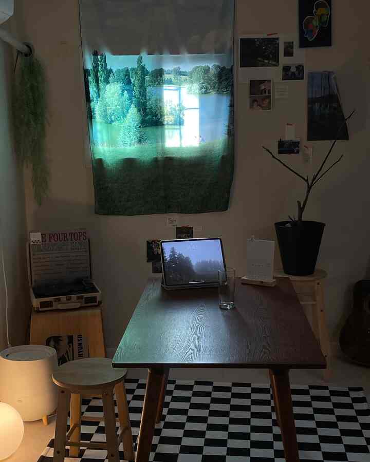 薄暗い照明の下、チェック柄ラグの上に木製テーブルとスツールが配置されたヴィンテージ感のあるホームオフィス兼ダイニング空間