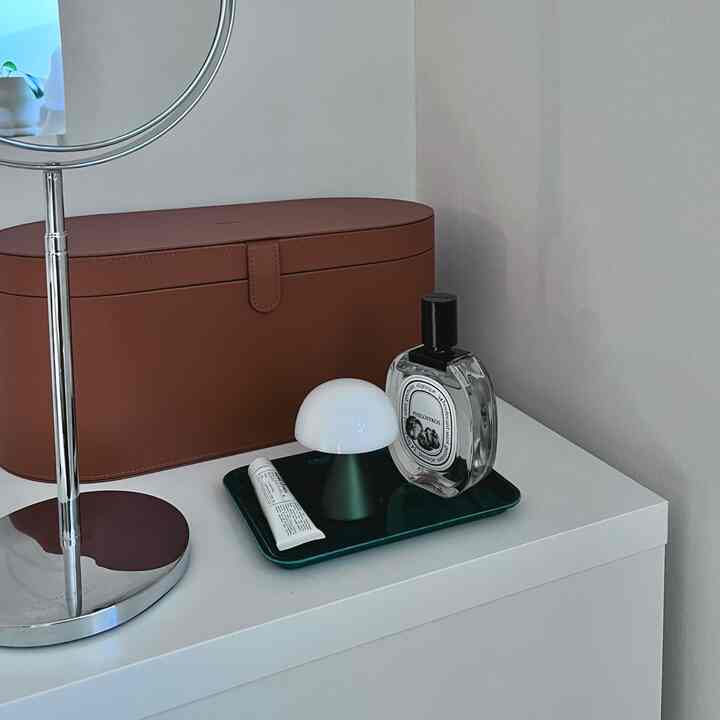 白を基調とした背景にブラウンの引き出しボックスとトレーの小物が配置されたシンプルな化粧台の空間