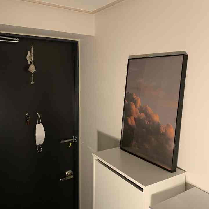 白と黒のトーンのモダンで清潔感のある玄関、雲のポスター額が置かれたシューズラックが特徴の空間