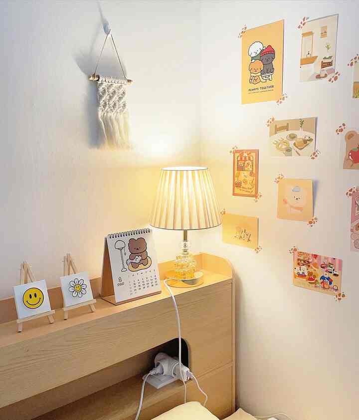 明るい白い壁とナチュラルな木の家具、かわいいポストカードとヴィンテージ風のテーブルランプがある温かみのある部屋の一角