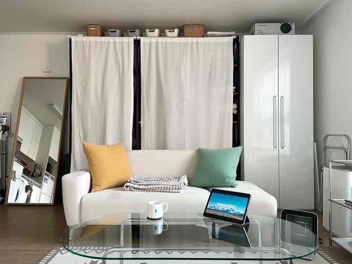 白を基調としたリビング、白いソファとクローゼット、カーテンで整えられた収納スペースのある印象的な空間