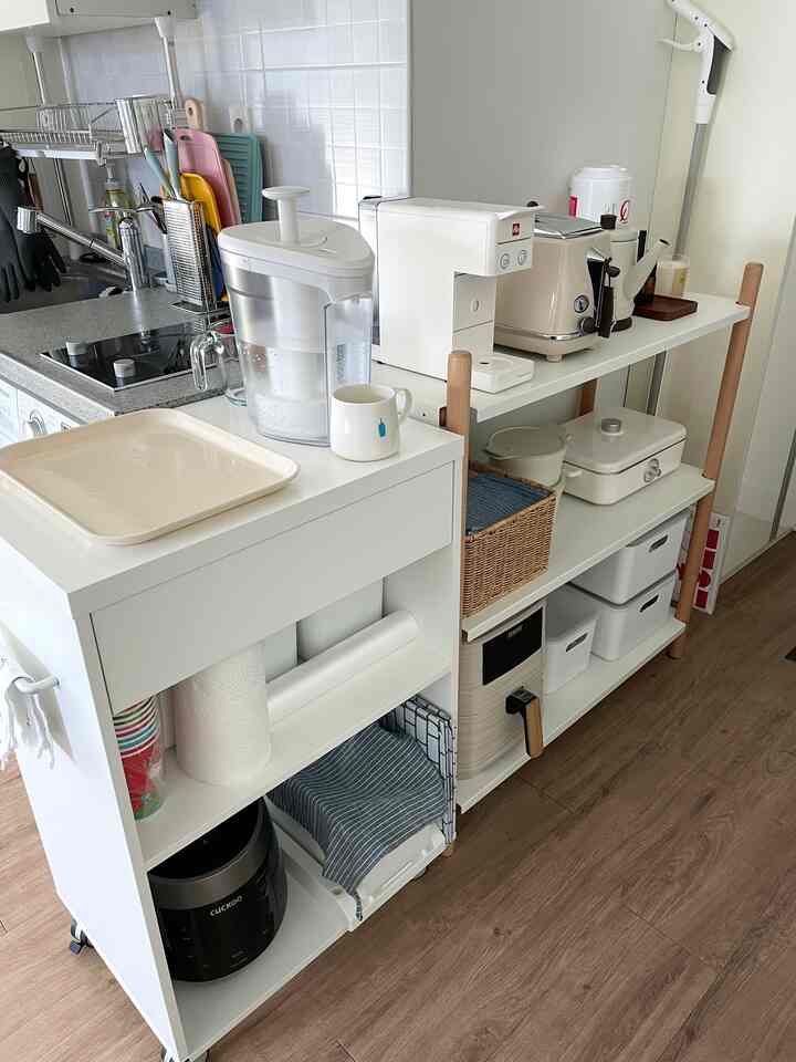 ホワイトとナチュラルウッドトーンが調和したコンパクトなキッチン空間、移動式キッチンカートと整理された収納棚が配置された実用的なインテリア