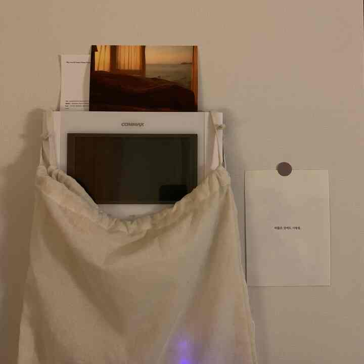 ナチュラルなベージュとホワイトトーンの玄関、コットンバッグで覆われたインターホンと壁に貼られたポスターがある雰囲気のあるインテリア