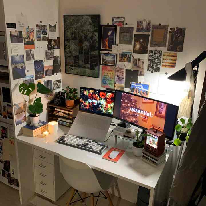 白を基調とした一人暮らしのホームオフィスで、デスクやモニター、植物、ポスターが配置された雰囲気のある作業空間