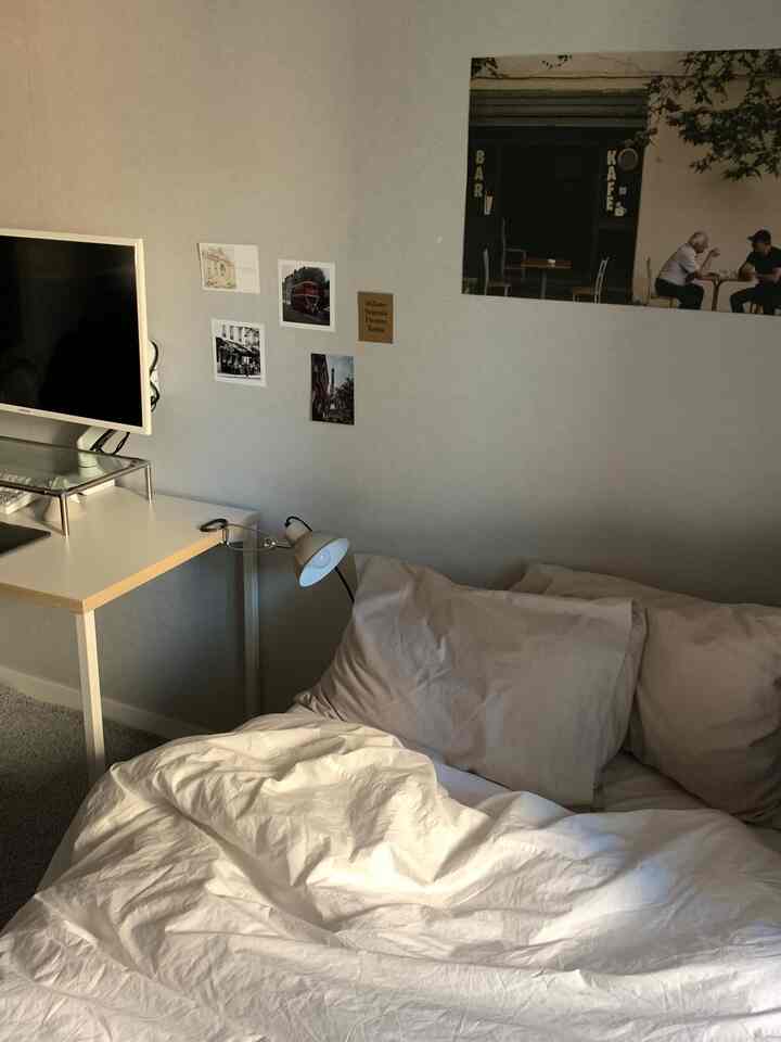 白とグレーのトーンのワンルーム寝室、デスクとモニター台が配置されたシンプルでモダンなインテリア