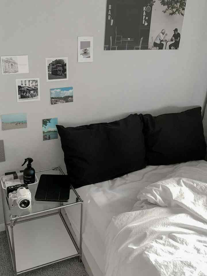 白い壁と寝具、黒い枕カバーとモジュールサイドテーブルが配置された落ち着いたワンルーム寝室のインテリア