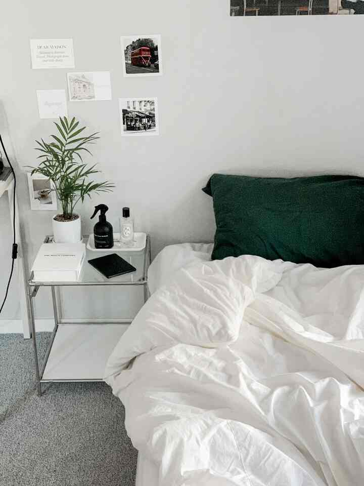 白い寝具と緑の枕があるワンルーム寝室、植物のあるナイトテーブルが配置された清潔感のあるモダンなインテリア
