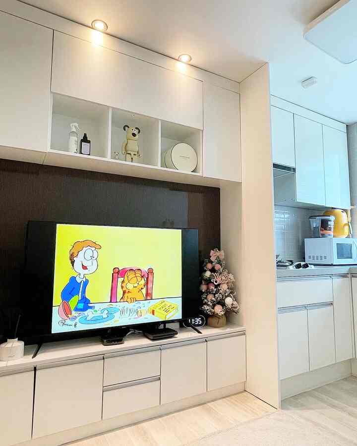 ホワイトトーンのリビングとキッチンが続く空間、シンプルな家具とテレビ台が配置された雰囲気のあるインテリア