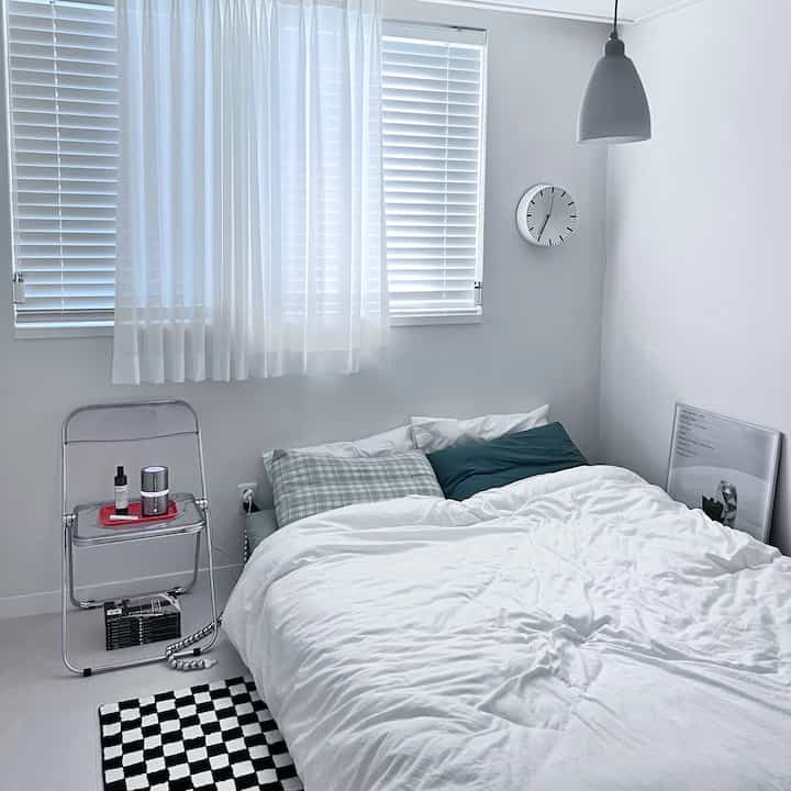 ホワイトと透明感のある素材が調和したワンルームの寝室、シンプルな家具とカーテン、ブラインドが配置された落ち着いたインテリア