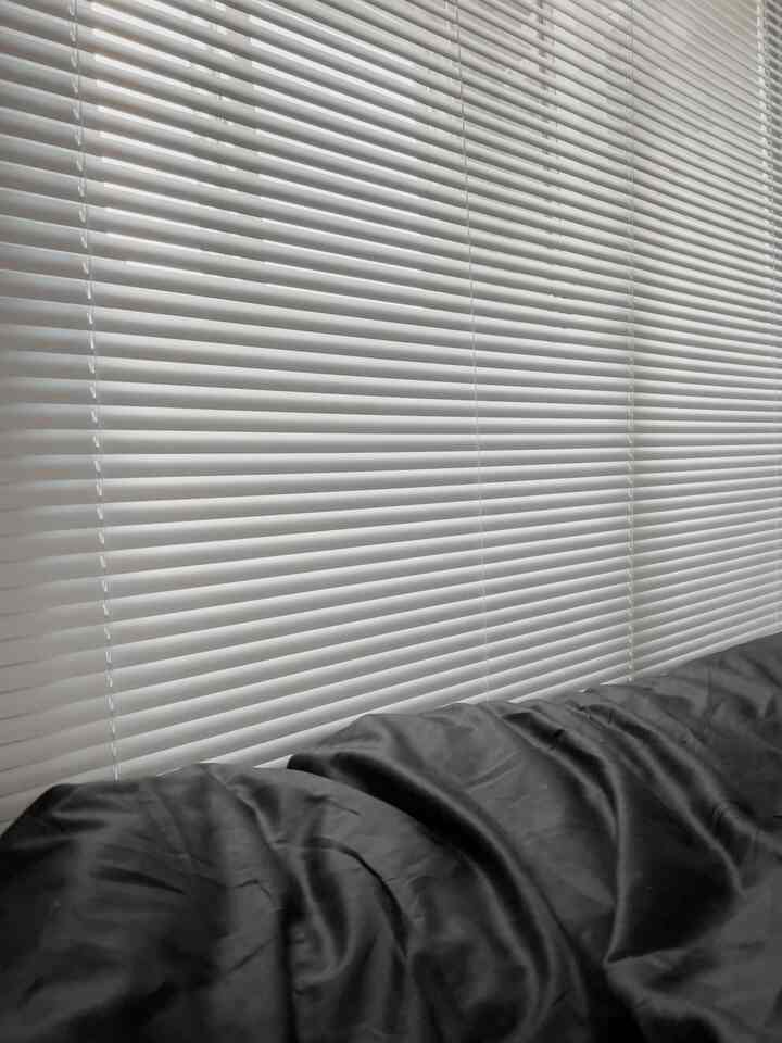 白いアルミブラインドと黒い掛け布団カバーがあるワンルーム寝室のモノトーンで落ち着いたインテリア