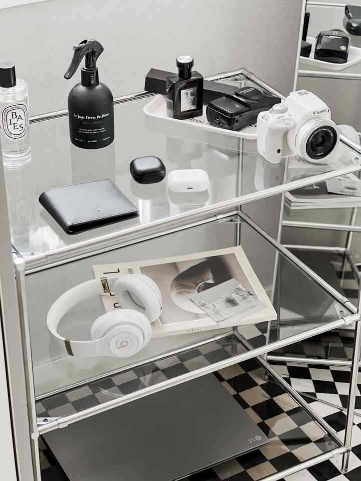 白と黒のトーンの透明なモジュール式キャビネットが配置されたワンルーム、電子機器やカメラアクセサリーが整頓されたミニマルな空間