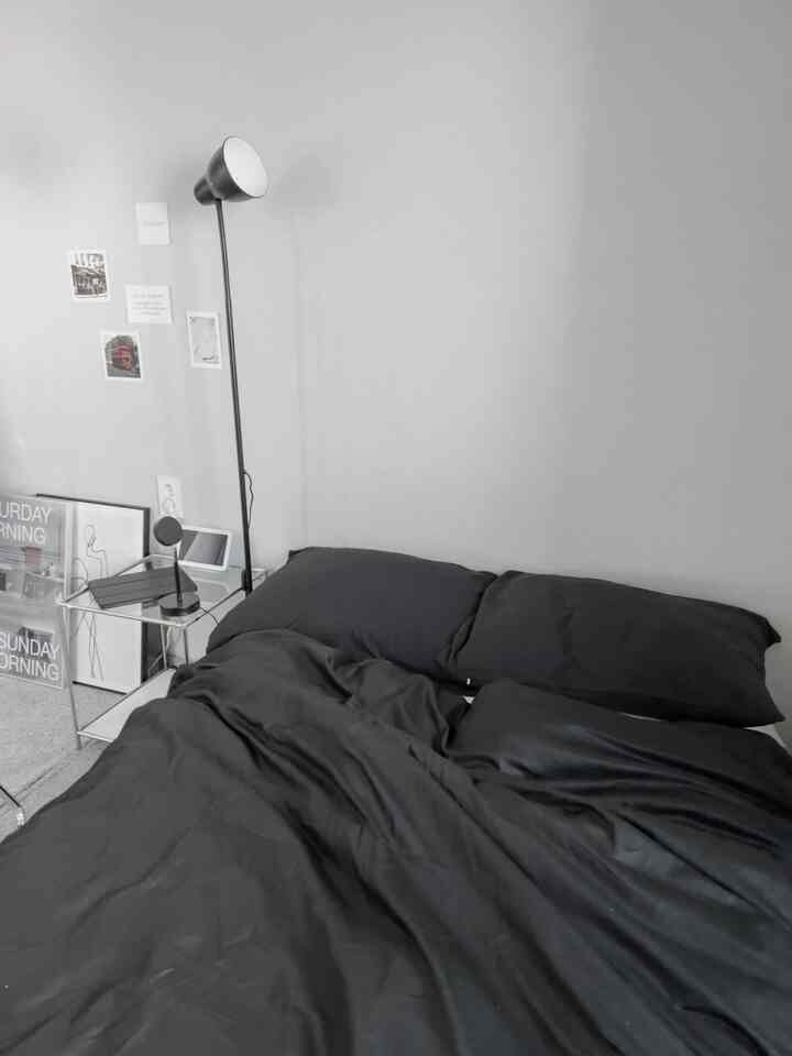 モダンなモノトーンの寝室、黒い掛け布団カバーと枕にフロアランプとサイドテーブルが配置されたすっきりとした空間