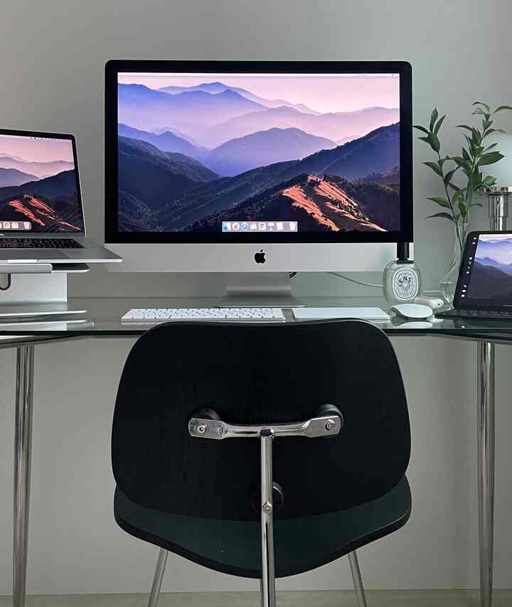 白い壁と透明なガラスデスクが特徴のモダンなホームオフィス、黒いオフィスチェアが配置された整った作業空間