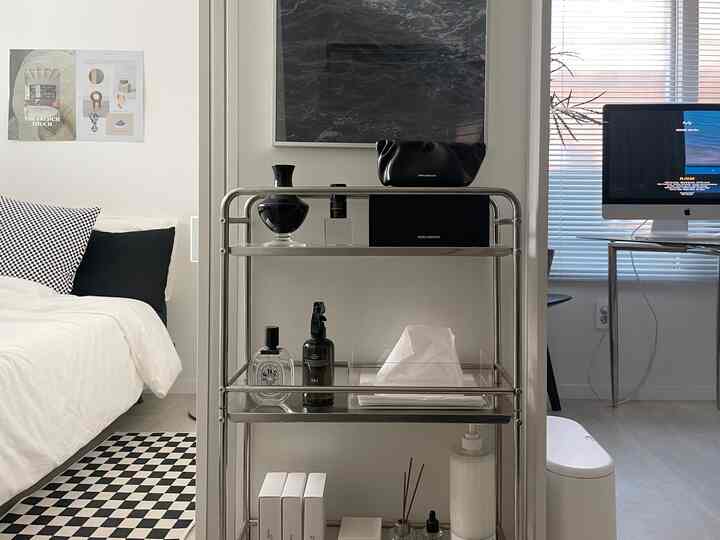 白と黒のトーンが調和した小さなリビング、ステンレスのワゴンとチェッカーパターンのラグが配置された印象的なインテリア