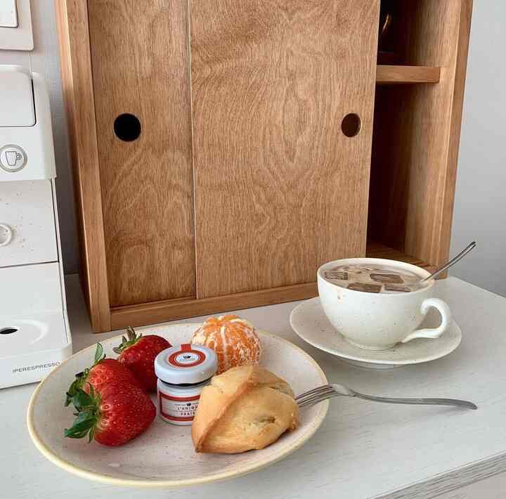 白とナチュラルカラーのキッチンスペース、コーヒーマシンと果物やパンがのったテーブルが印象的なホームカフェの雰囲気