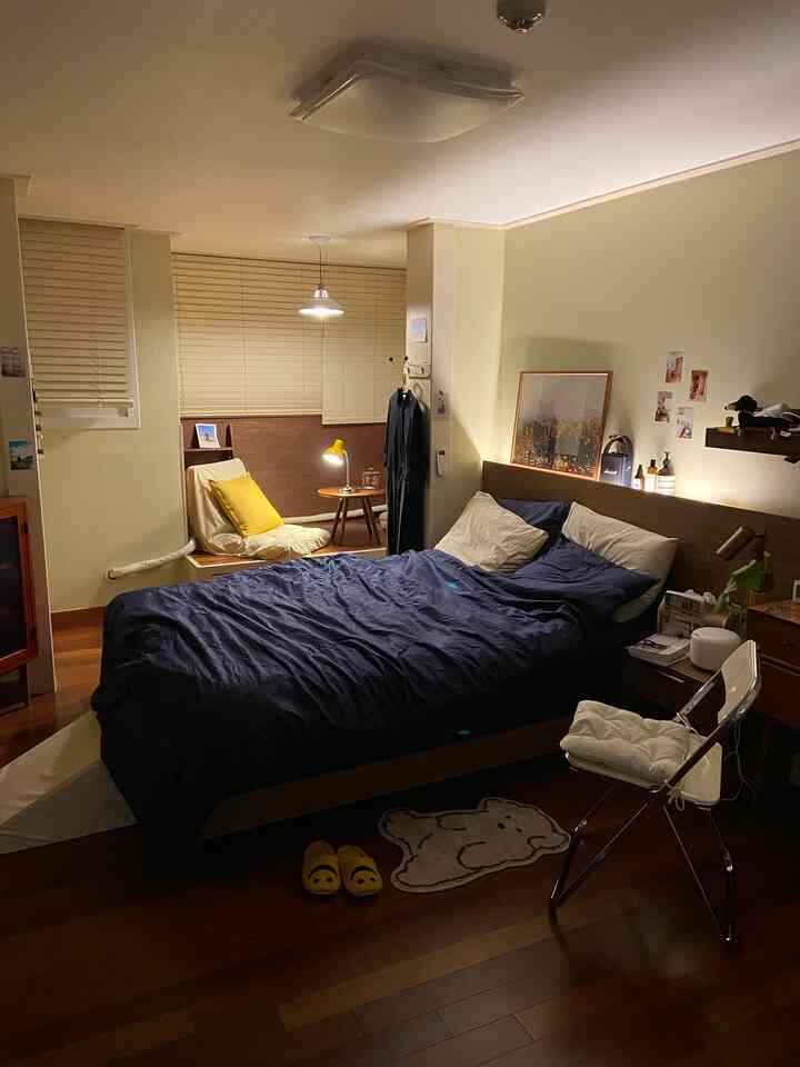 ネイビーとイエローの照明が調和したモダンな寝室、ナイトテーブルと椅子が配置された落ち着いた雰囲気の空間