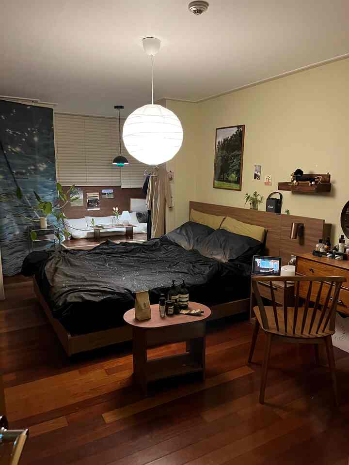 ベージュの壁と木目調の床が調和した寝室、黒い寝具とペンダントライトが印象的な雰囲気のあるインテリア