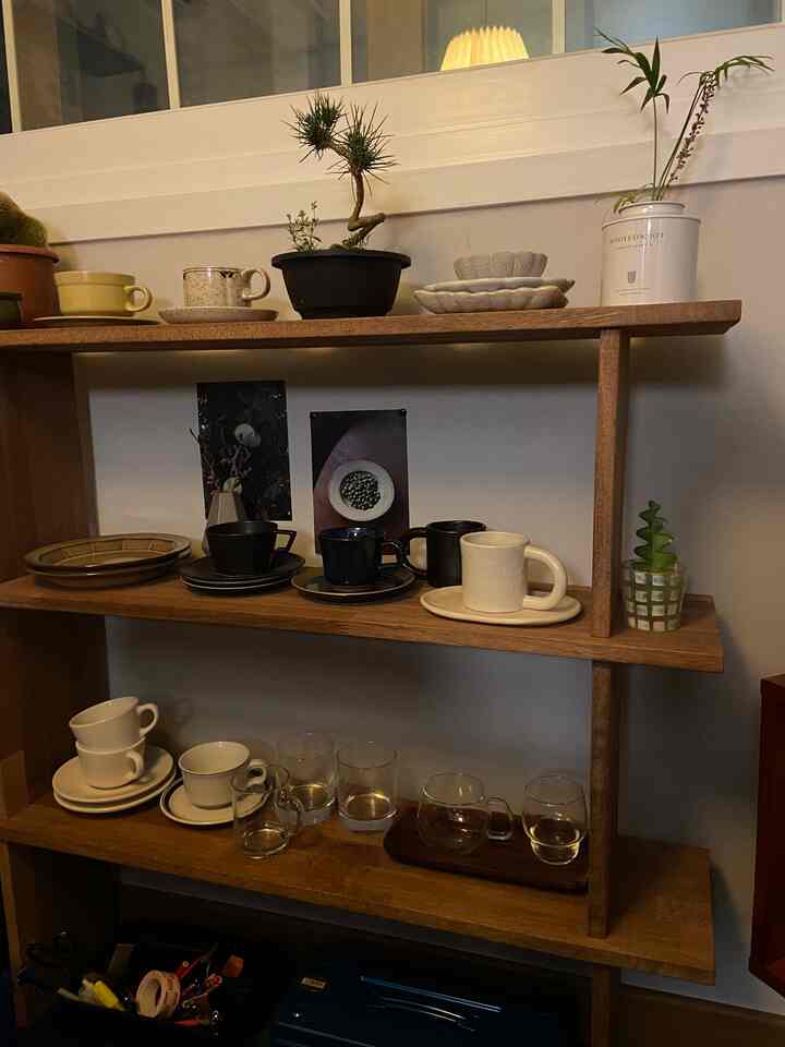 ナチュラルな木目調の棚にカップやマグ、植物が配置されたカフェ風の居心地の良い空間