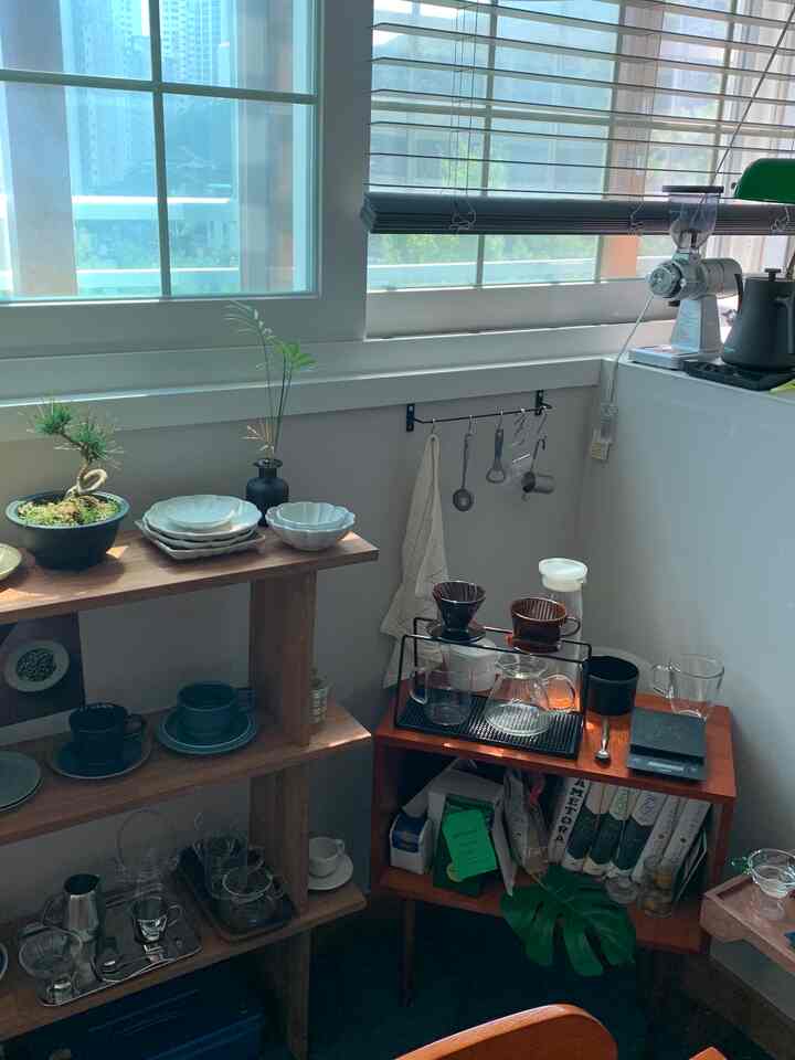 白い壁の狭いワンルームに、ブラウンの木製棚とチェストが置かれ、ハンドドリップコーヒーセットが配置された温かみのあるおうちカフェ